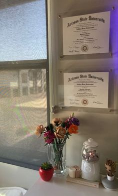 flowers are sitting in a vase next to two diplomas on the wall behind them