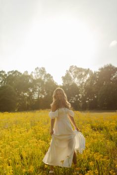 a woman in a white dress is walking through a field with yellow wildflowers