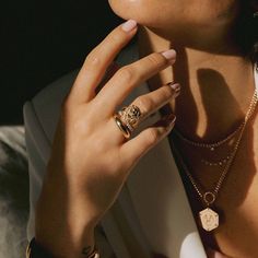 a close up of a person wearing rings and necklaces on their fingers, with one hand near her face