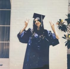 a woman wearing a graduation cap and gown holding her hands up in the air with one hand