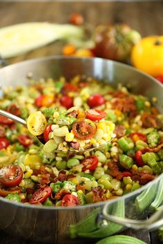 a spoon full of corn salad with tomatoes and green beans on the table next to other vegetables