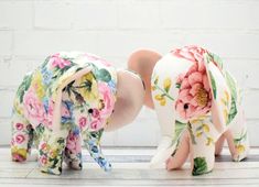 two ceramic elephants sitting next to each other on top of a wooden floor in front of a white brick wall