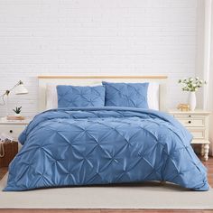 a bed with blue comforter and pillows in a room next to a white brick wall