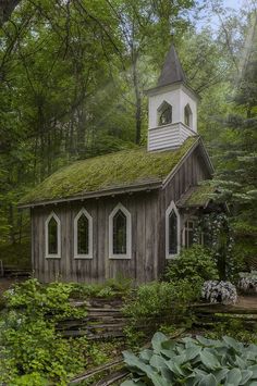 an old wooden church in the woods with a green roof and steeple on top