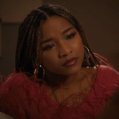 a woman with dreadlocks wearing a red top and large hoop earrings looking at the camera