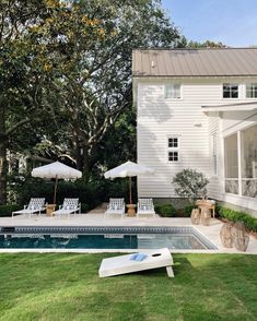 an empty swimming pool with lawn chairs and umbrellas in front of the house on a sunny day