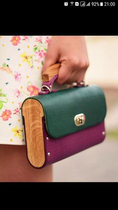 a woman is holding a green and purple handbag with wood accents on the handle