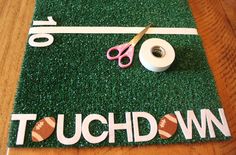 a pair of scissors and some tape on top of a green door mat that says touchdown