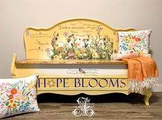 a yellow bench with flowers on it and two decorative pillows next to it that say, hipe blooms