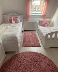 two twin beds in a small room with pink rugs on the floor and windows