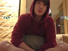 a young man sitting on top of a bed wearing a red hoodie and bracelet