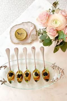 five spoons with small cakes on them sitting on a plate next to flowers and a vase