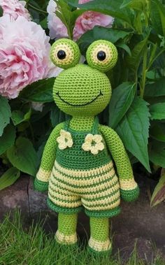 a crocheted frog is standing in front of some flowers