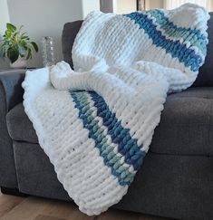 a white and blue blanket sitting on top of a gray couch next to a potted plant