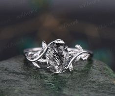 a white gold engagement ring with an oval cut diamond surrounded by leaves on a rock