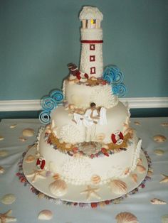 a three tiered wedding cake is decorated with seashells and a lighthouse on top