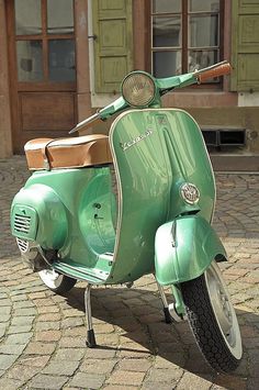 a green scooter parked on the side of a brick road next to a building