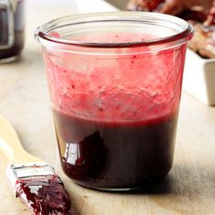 a jar filled with red liquid next to a wooden spoon