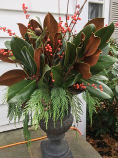 a vase filled with red berries and greenery on top of a cement block next to a house