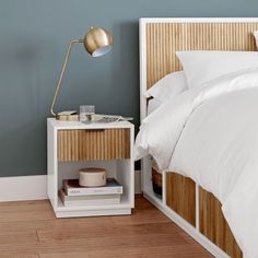 a bed with white sheets and pillows in a bedroom next to a nightstand with a lamp on it