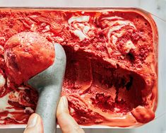 a hand holding a spatula over a red dessert in a pan with ice cream