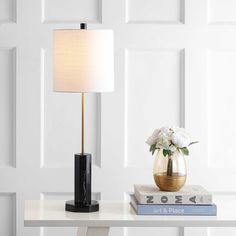 a table with a lamp, books and flowers on it in front of a white wall