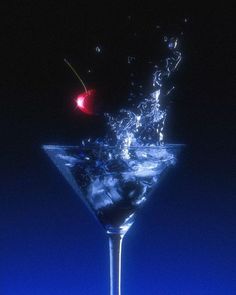 a martini glass filled with water and a cherry on the rim, in front of a blue background