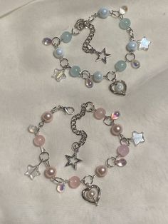 two bracelets with charms on them sitting on a white cloth covered tablecloth in the shape of hearts and stars