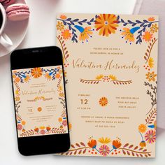 an orange and yellow floral wedding card next to a smart phone on a white table