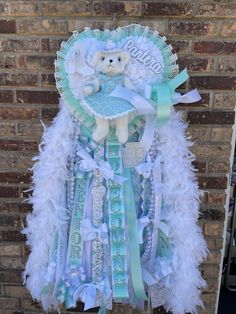 a teddy bear hanging on the side of a brick wall with white and blue feathers