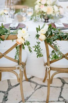 two wooden chairs sitting next to each other on top of a table with flowers and greenery