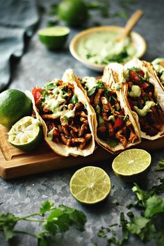 several tacos on a cutting board with limes and cilantro