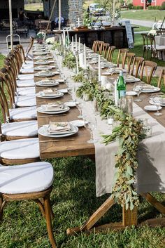 a long table is set with place settings and greenery for an outdoor dinner party