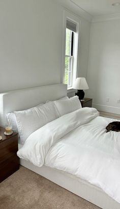 a large bed with white sheets and pillows in a bedroom next to a lamp on a dresser