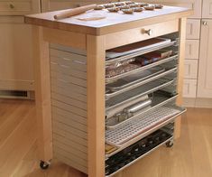 a kitchen island with drawers and trays on it in the middle of a wooden floor