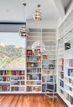 a room with many bookshelves and hanging lights in it, along with a ladder to the ceiling