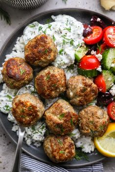 meatballs and rice on a plate with lemon wedges, tomatoes, cucumber, cherry tomatoes, cucumber salad