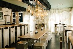 an empty dining room with wooden tables and white chairs, hanging chandelier over the table