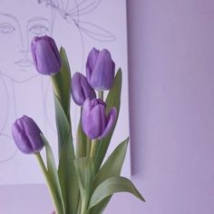 purple tulips are in a vase on a table next to a wall drawing