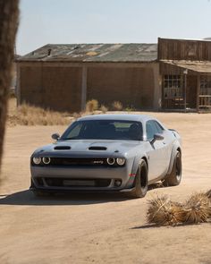 a white car parked in the middle of a dirt lot next to a building and palm tree