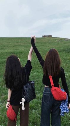 two women standing in the grass holding their arms up and looking at an old building