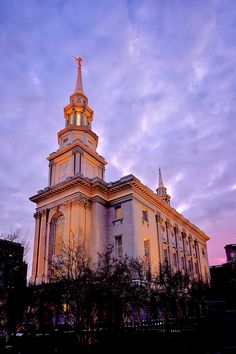 a large building with a steeple on top in the evening time, lit up by street lights