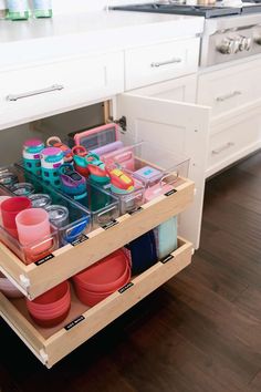 an open drawer in a kitchen filled with plastic containers and bowls on top of wooden flooring