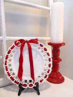 a plate with a red ribbon on it next to a candle