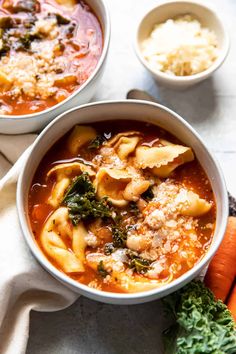 two bowls filled with pasta and spinach soup on top of a white table cloth