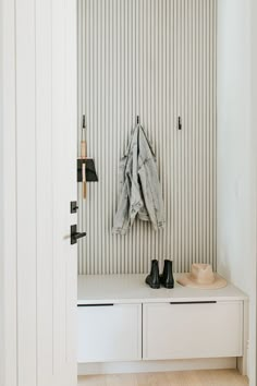 a coat rack with shoes and jacket hanging on it's hooks in a white entryway