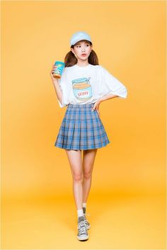 a girl in a skirt and hat holding a can of coffee while standing on a yellow background