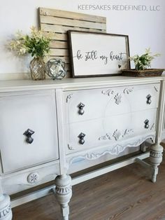 a white dresser with some flowers and a sign above it that says, be still my heart