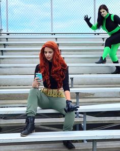 a woman sitting on bleachers holding a cell phone in her hand and another person standing behind her