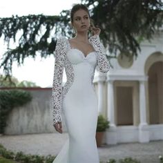 a woman in a white wedding dress with long sleeves and lace on the top, standing outside